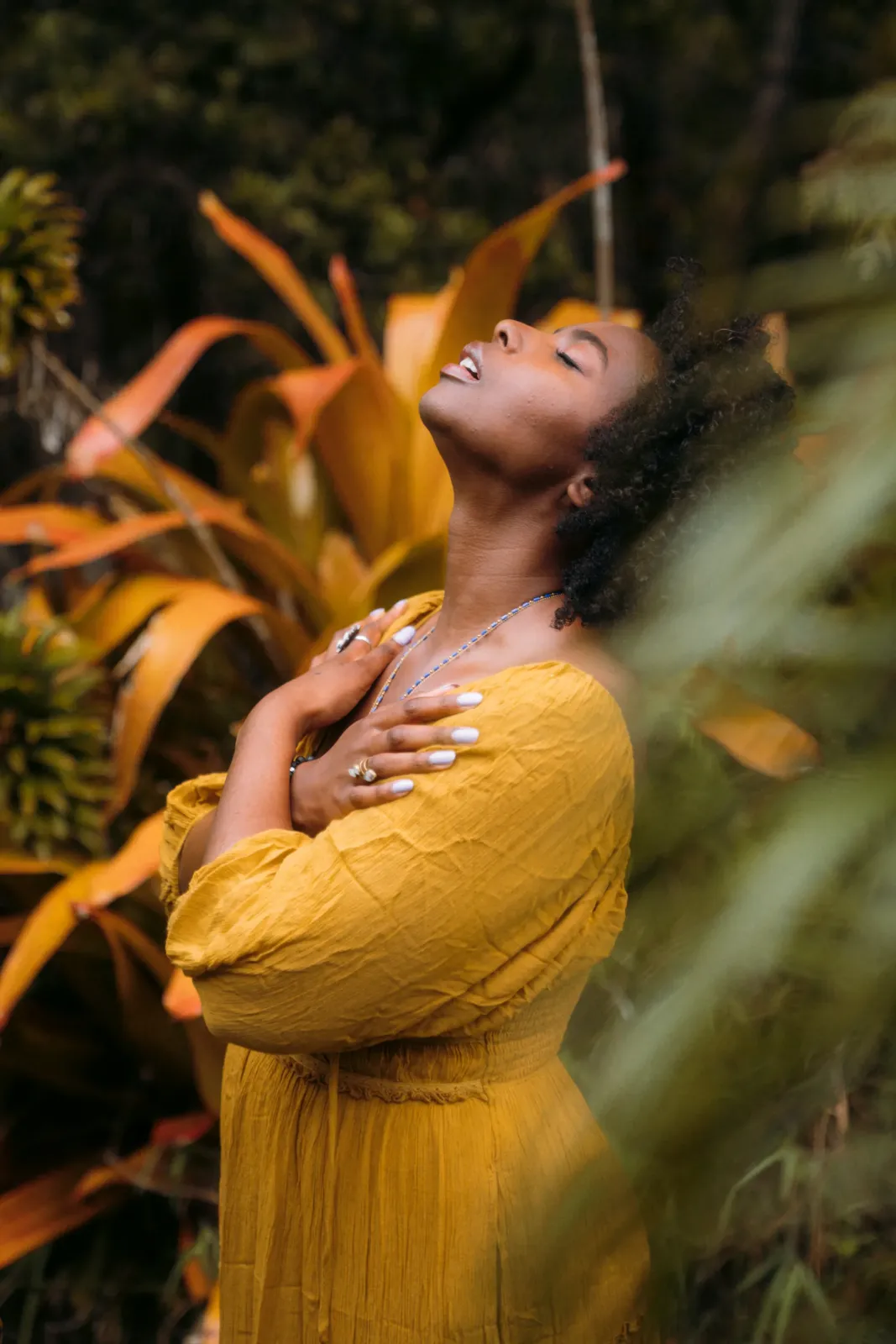 A woman in a golden dress with her head tilted back, arms crossed over her chest, breathing freely